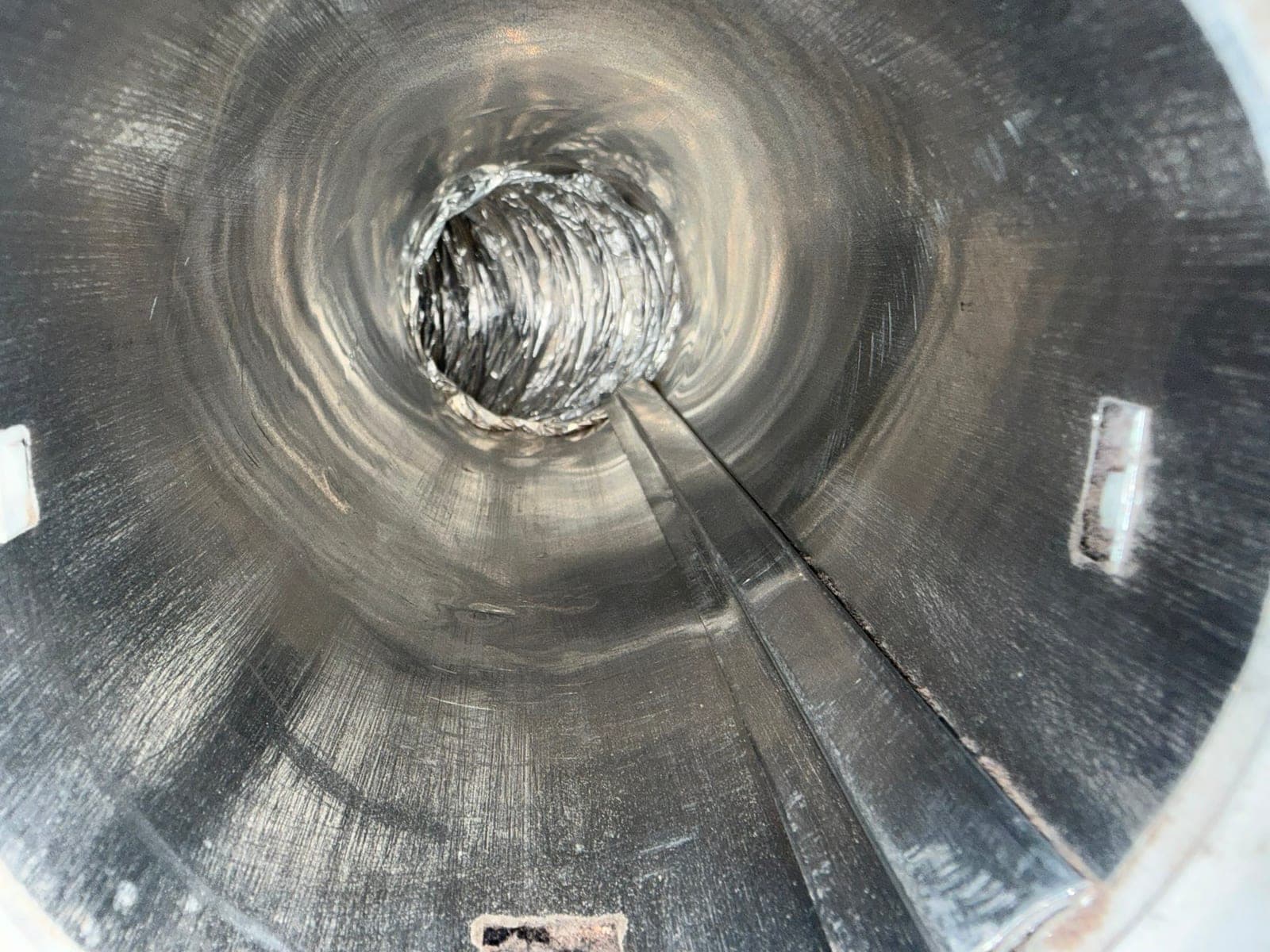 Interior view down a round metal duct after cleaning, showing clean bare metal walls and a flexible connection at the far end